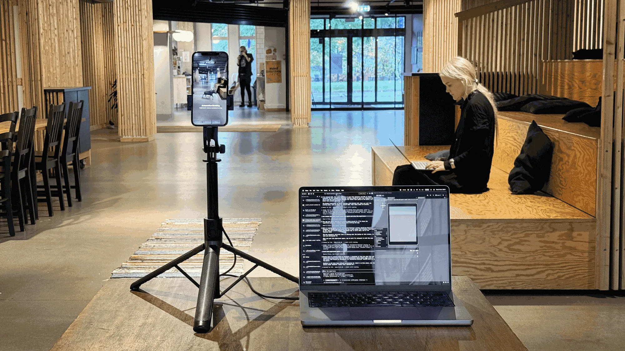An iPhone on a tripod pointing at the studio floor, with a laptop running Claude Code next to it